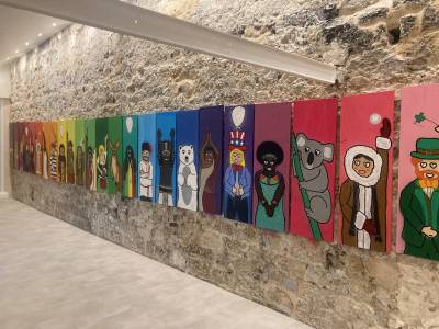 Dans une galerie des toiles petit format et colorées sont exposées sur un mur de pierre