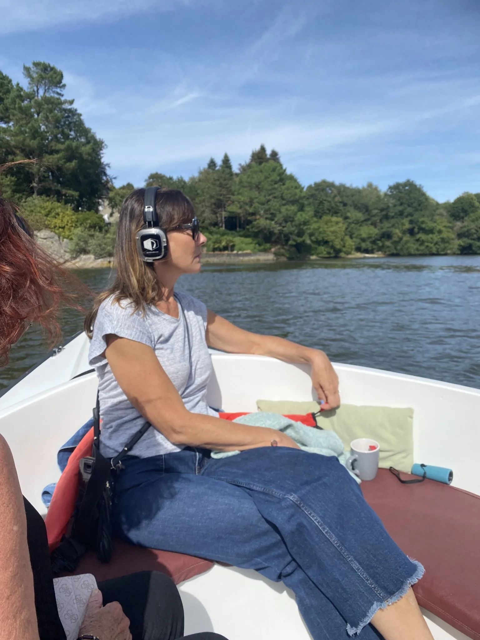 Une femme, casque audio sur les oreilles plonge son regard sur la ria de pont-Aven depuis le bateau sur lequel elle navigue.