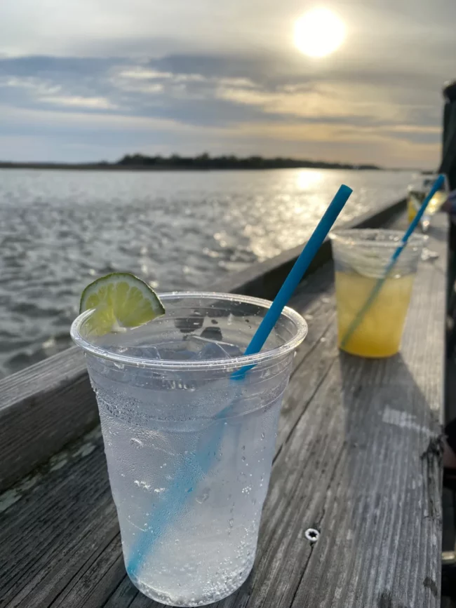 un verre posé sur une rembarde de bois au coucher de soleil.